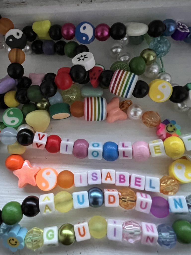 a line-up of colourful beads necklaces with names laying on a white table