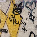 graffiti on a pale tan bridge underpass of a cat on a yellow diamond and some black lettering