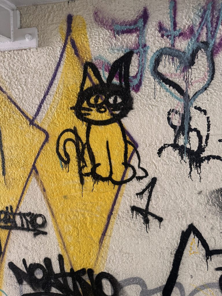 graffiti on a pale tan bridge underpass of a cat on a yellow diamond and some black lettering