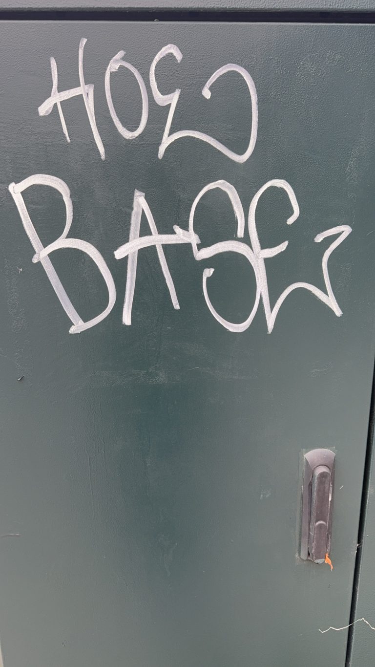 white graffiti on a dark grey electrical box that says hoe base