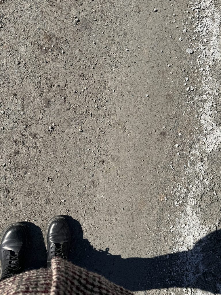 a pair of feet wearing boots with standing at the water's edge at the beach in the sand and there is a shadow to the right